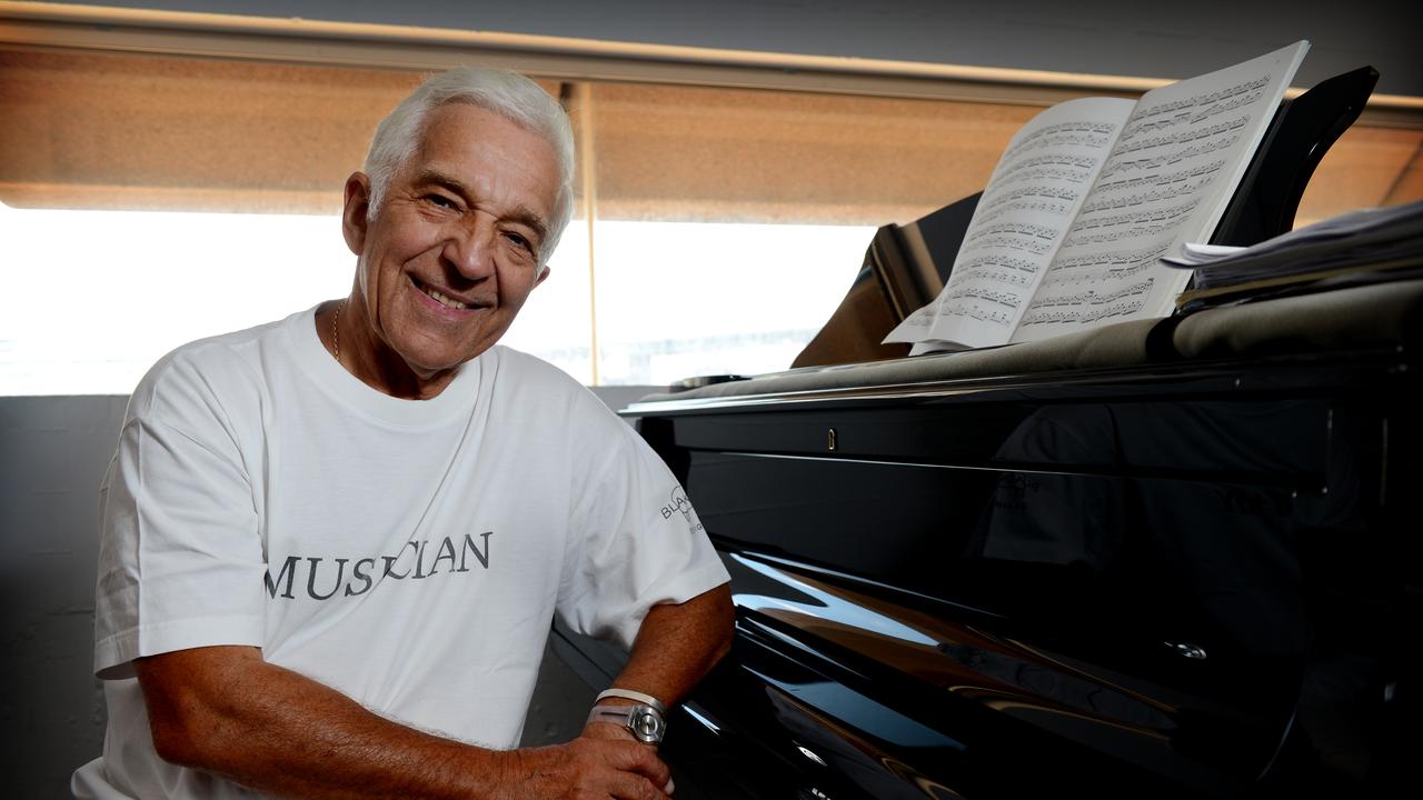 Pianist Vladimir Ashkenazy smiling next to a black grand piano with sheet music.