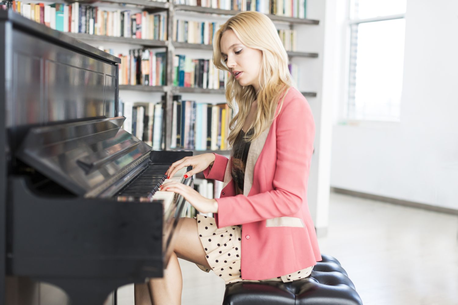 Blonde hair girl wears pink coat and playing piano