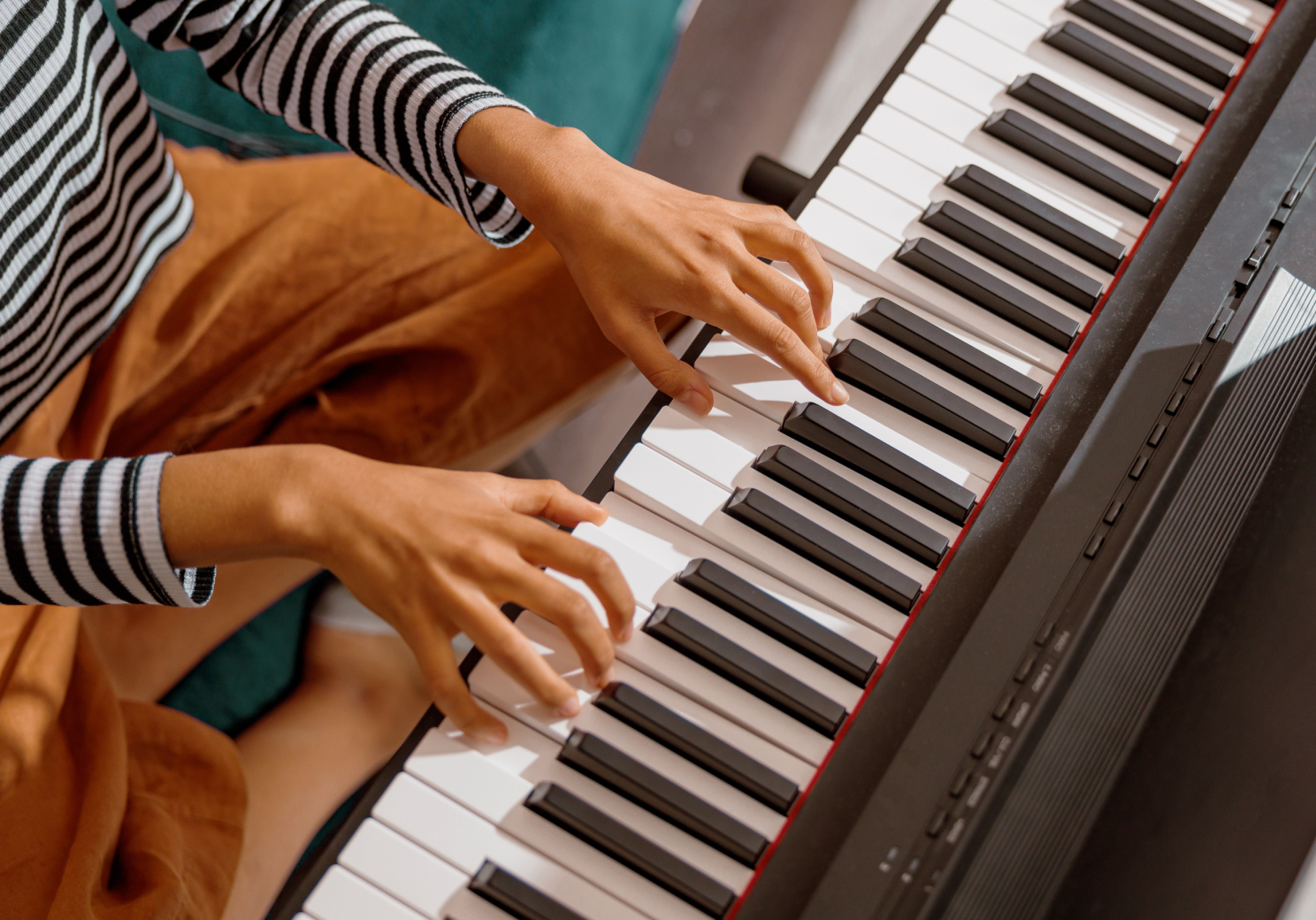 Close-up of hands playing keys on a digital piano with red trim and control panel on the right side