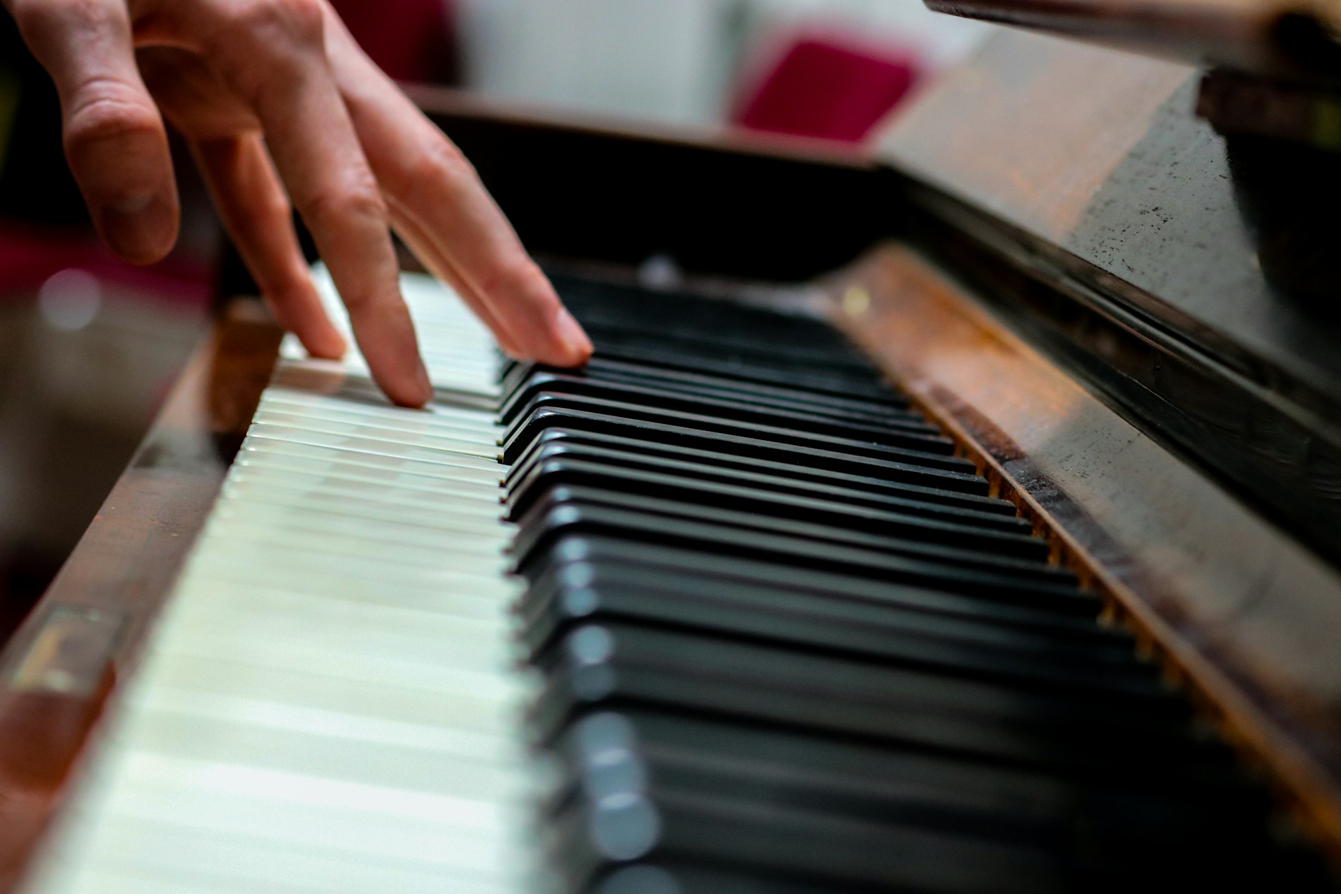 Close-up of fingers pressing piano keys on a wooden piano with blurred background and shallow depth of field