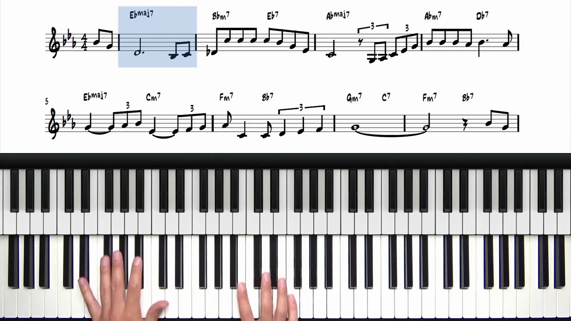 Overhead view of hands playing piano keys with sheet music and chord symbols displayed above the keyboard