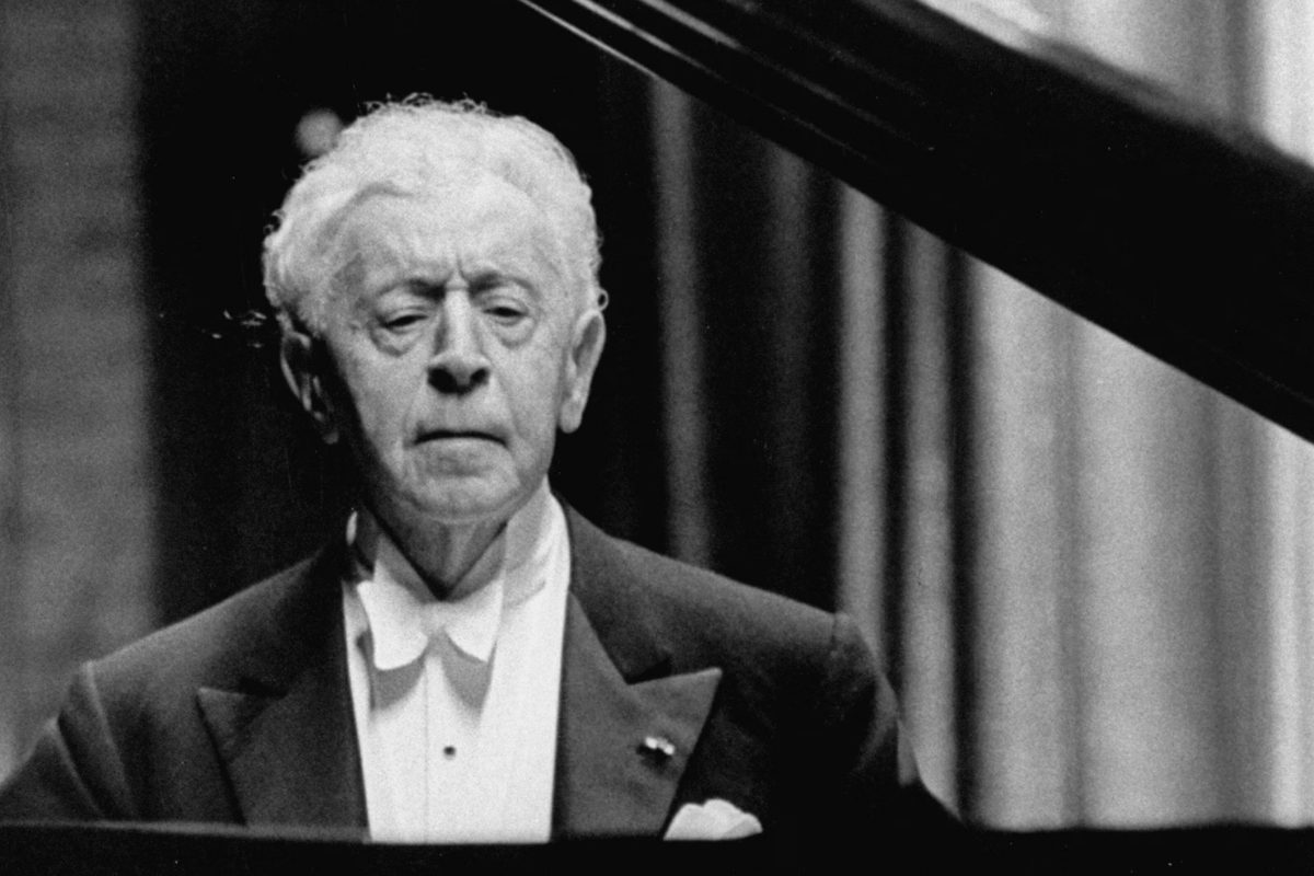 Elderly pianist performing beside grand piano in concert