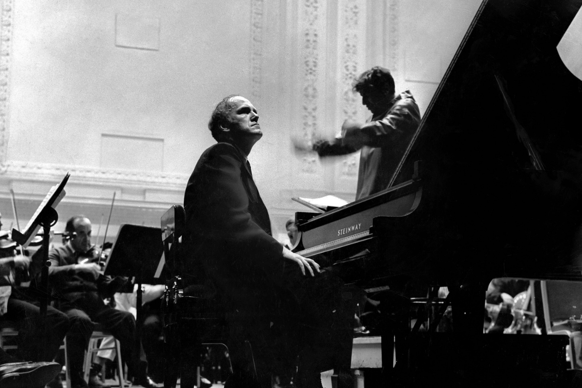 Pianist performing with orchestra beside grand concert piano