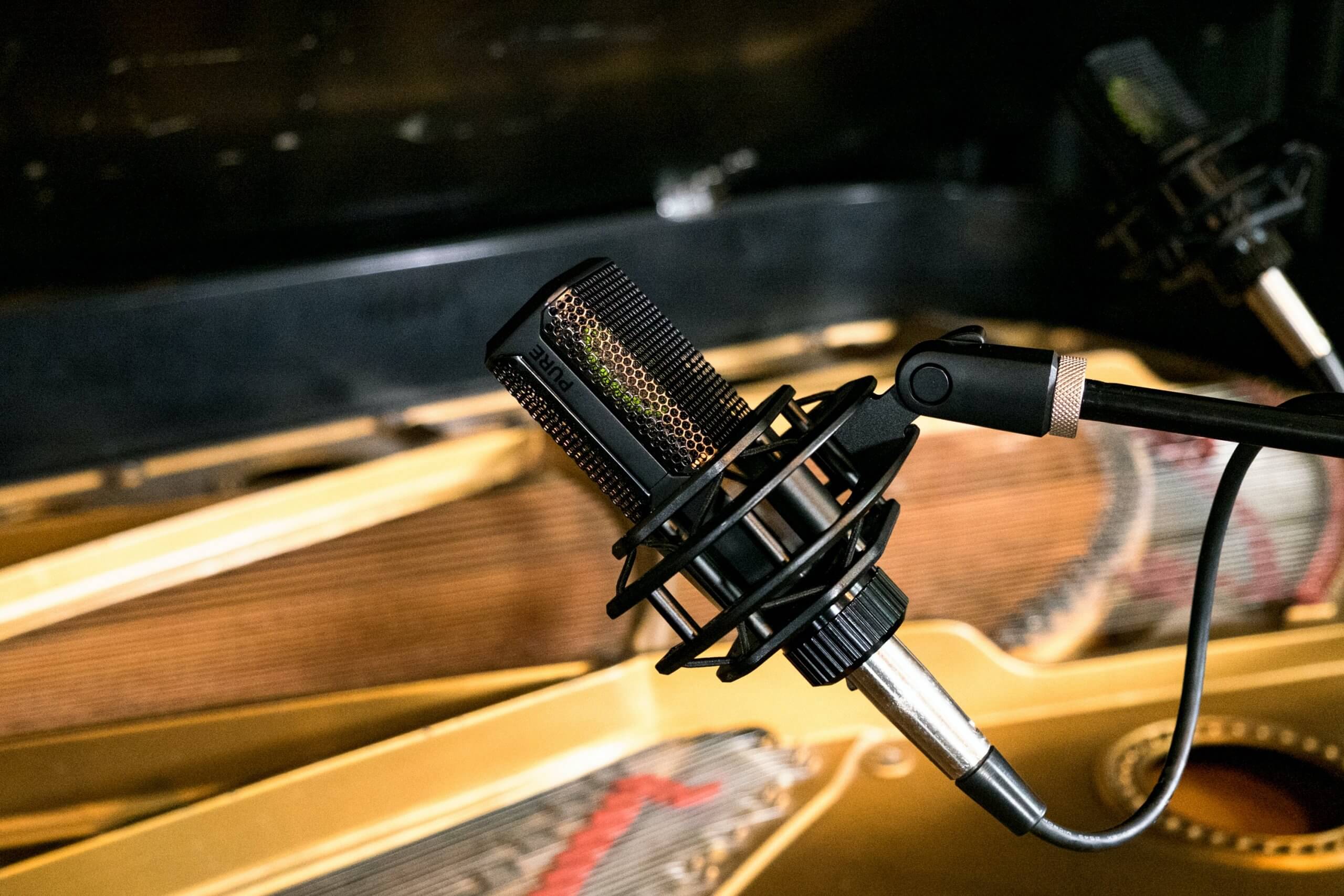 Close-up of a studio condenser microphone positioned above piano strings inside a grand piano