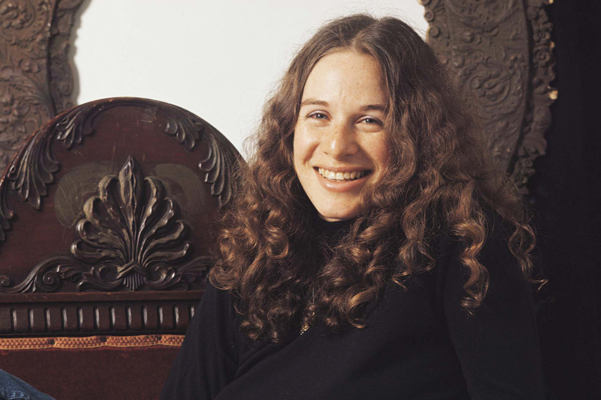 Smiling woman with curly hair seated beside ornate chair