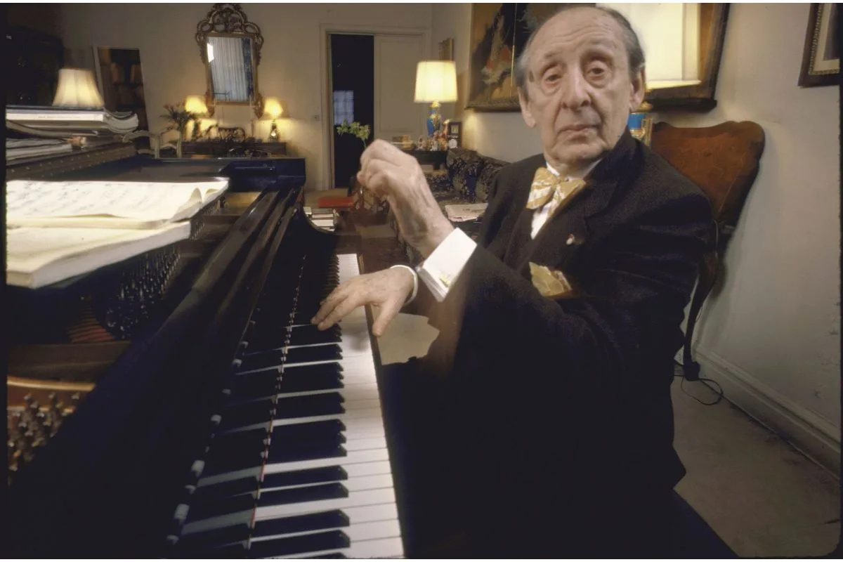 Elderly pianist seated beside grand piano indoors