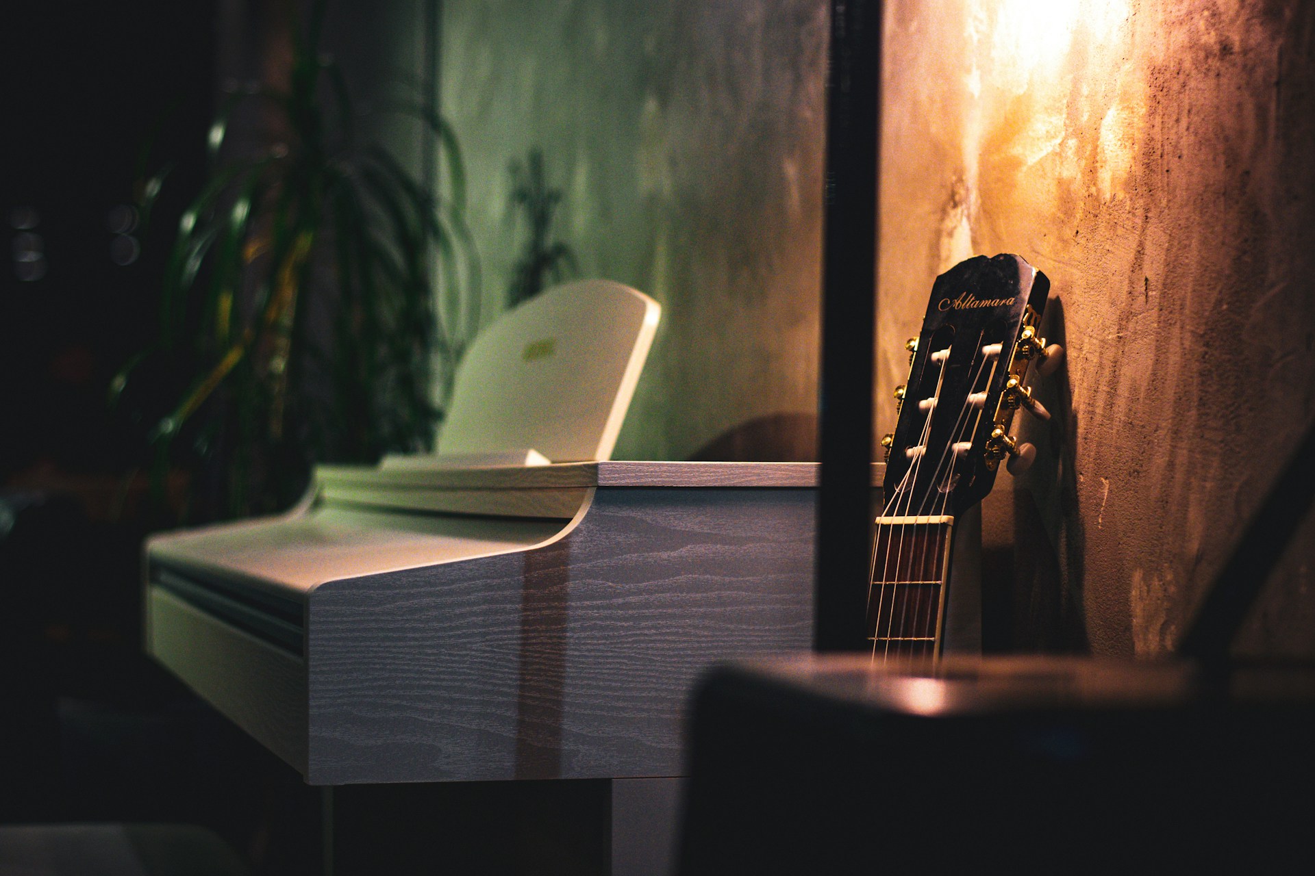 Acoustic guitar leaning beside a white piano in a softly lit room