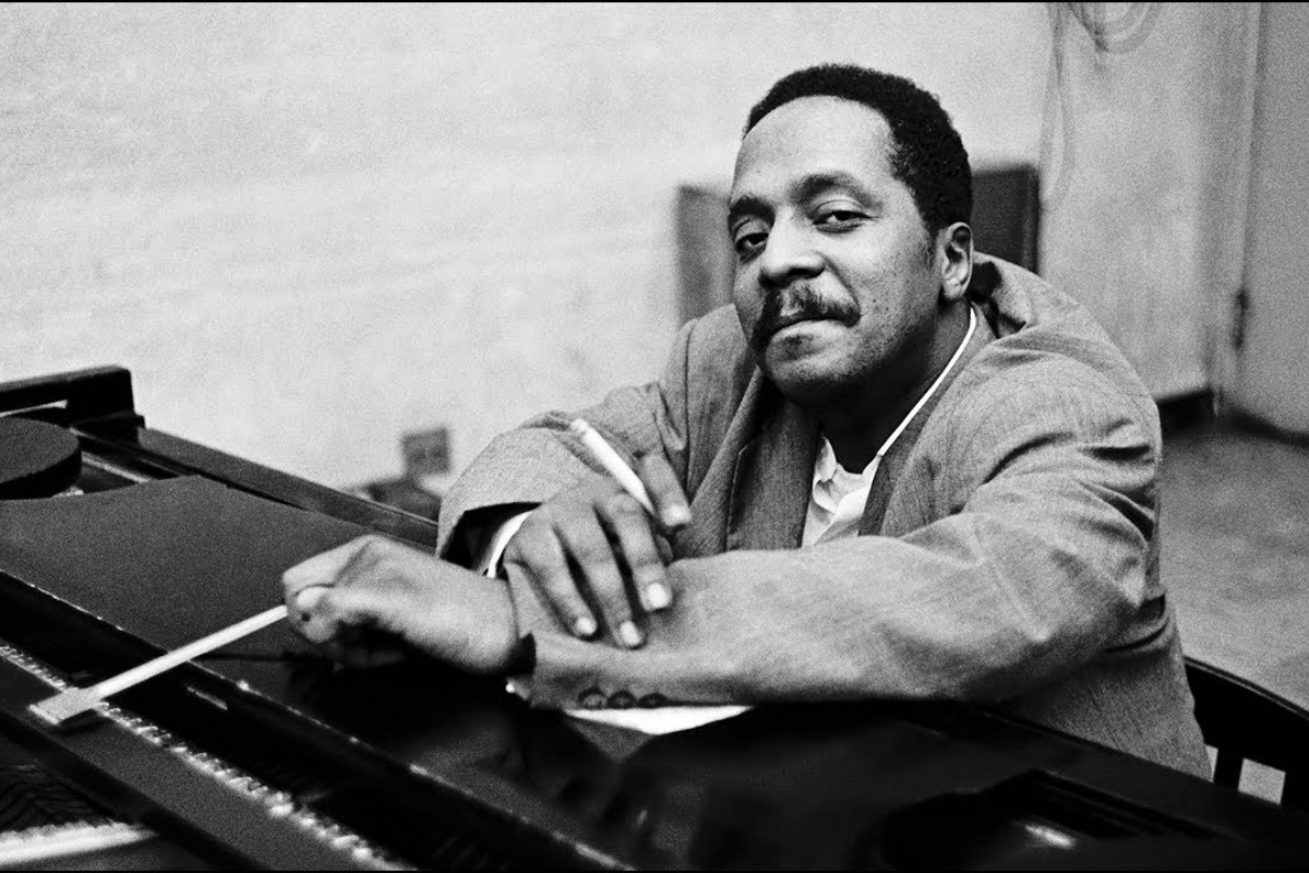 Jazz pianist leaning casually across grand piano keyboard