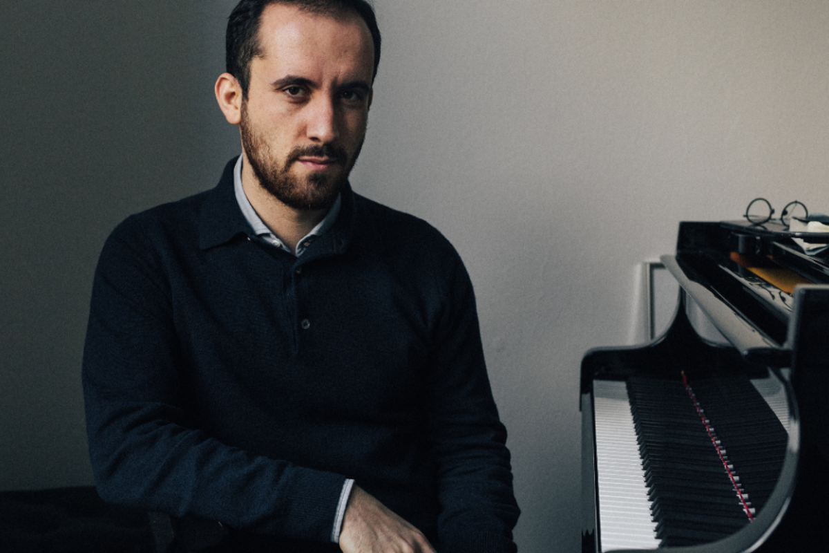 Bearded man seated beside grand piano indoors