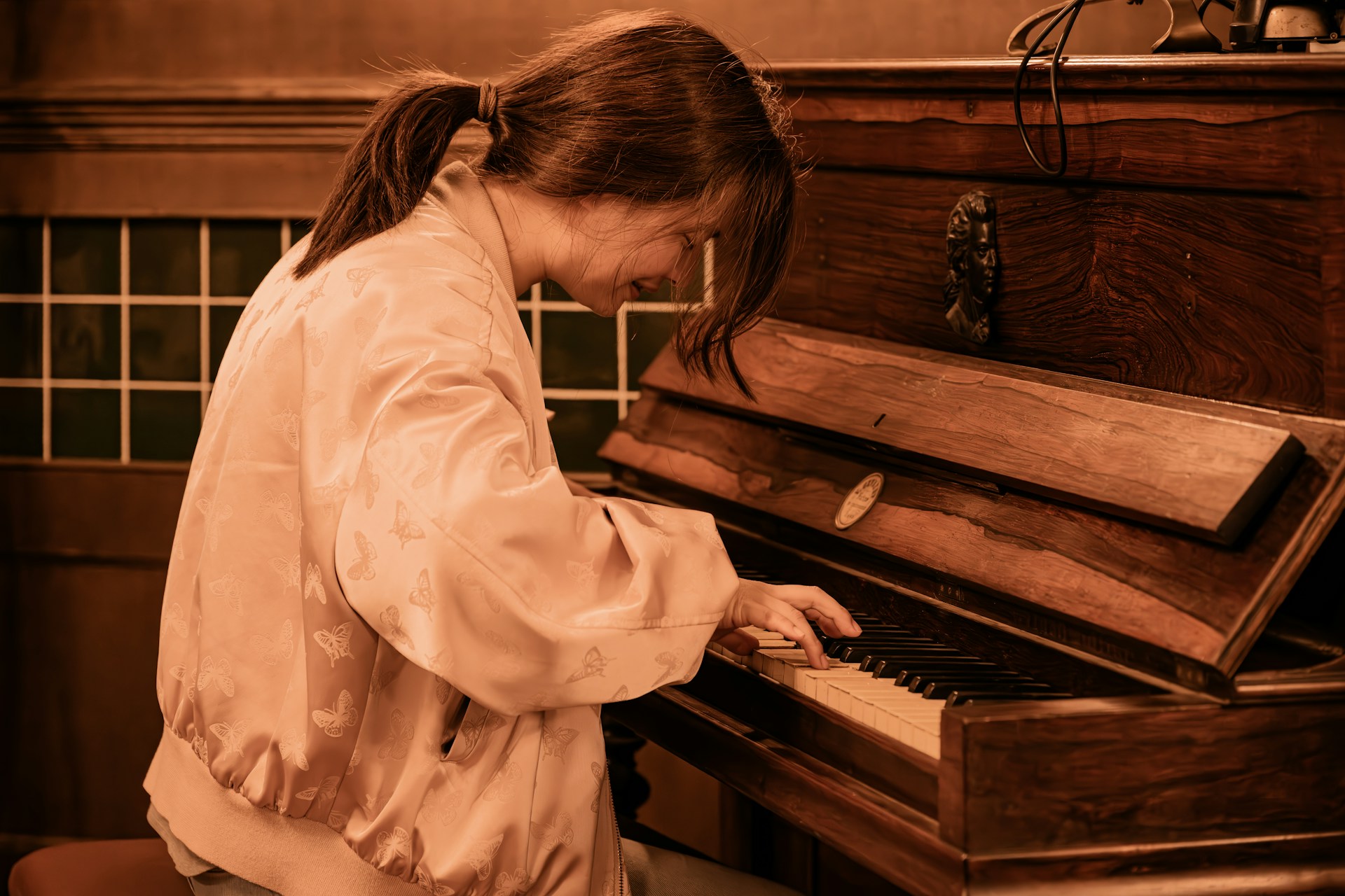A young woman playing a wooden upright piano while laughing
