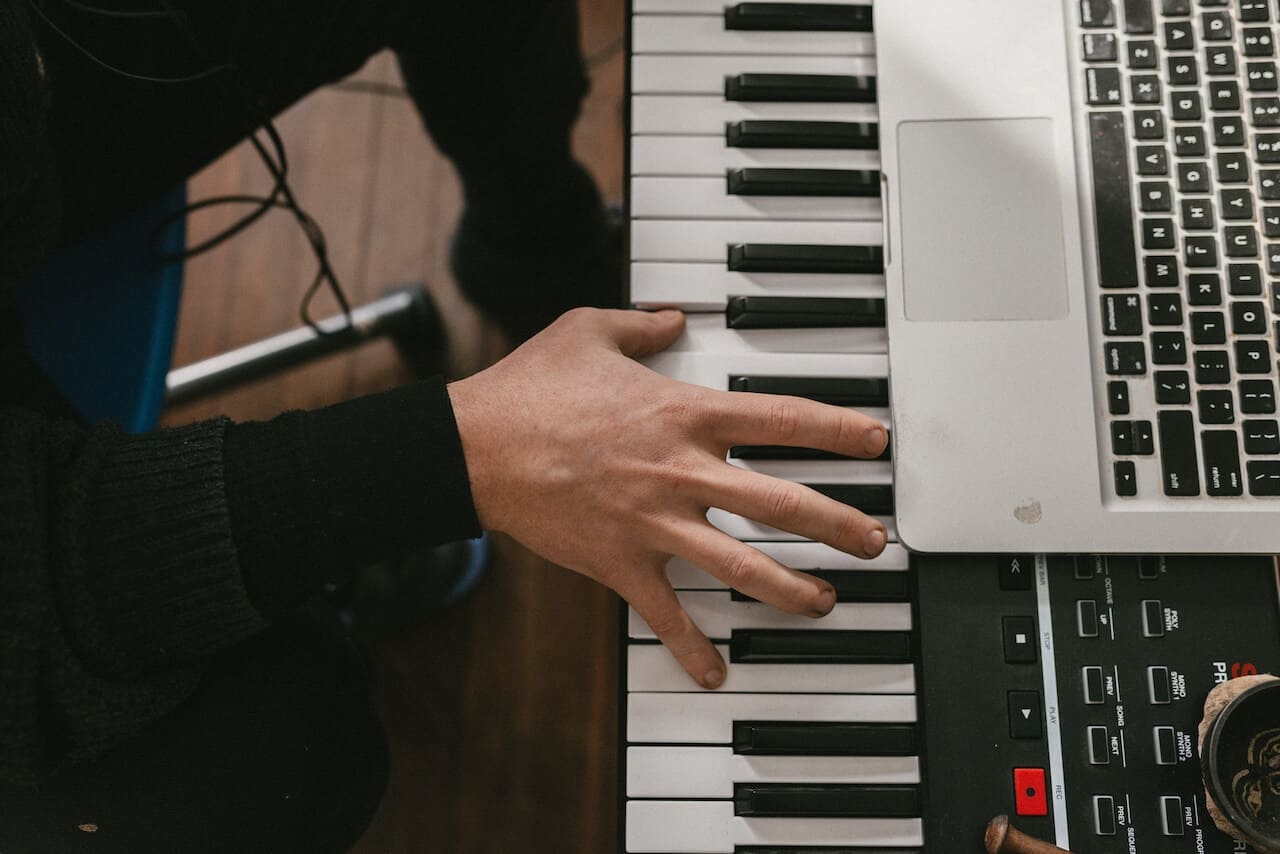 A home studio setup showing a hand playing a digital piano keyboard next to a laptop